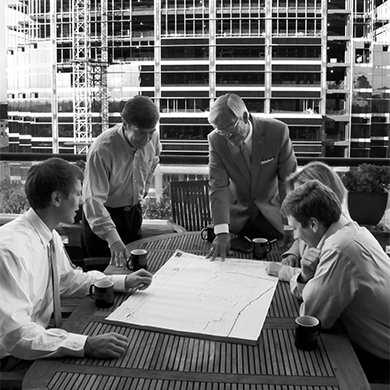 A black and white photo of the Seven Oaks Company staff having a conference outdoors while looking at planning documents.